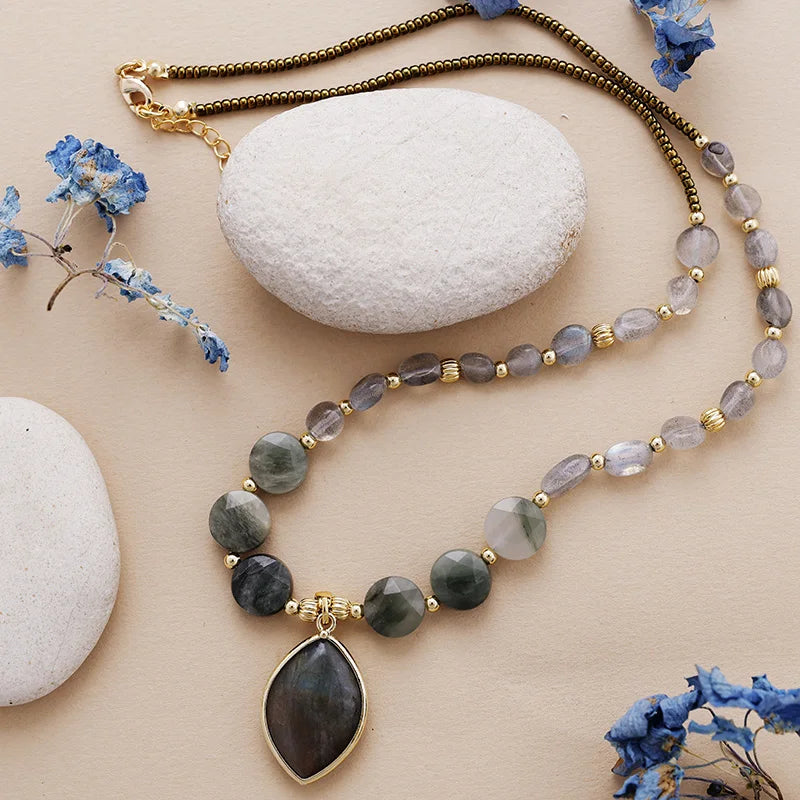 Beaded necklace with a pendant on a beige surface with stones and blue flowers.
