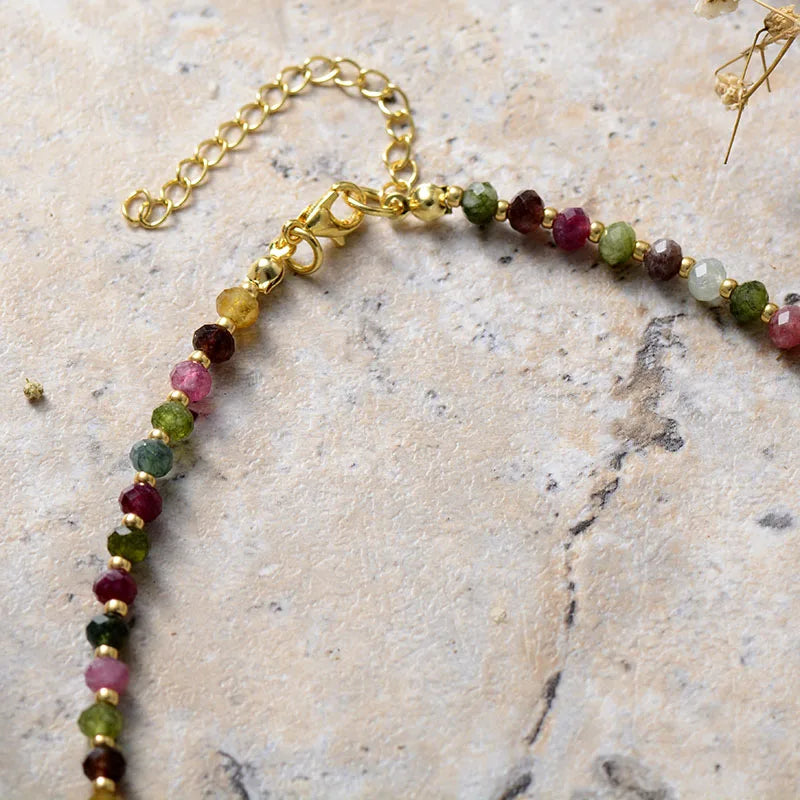 Necklace with multicolored beads and gold chain on a stone surface