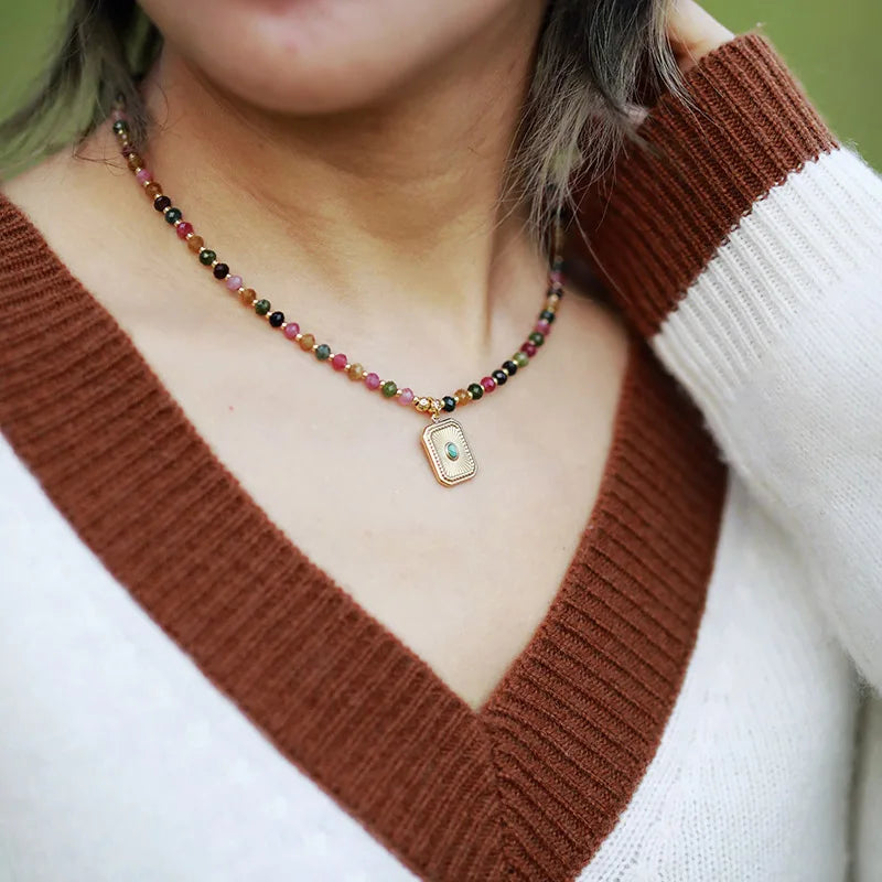 Person wearing a colorful beaded necklace with a pendant on a brown and white sweater.