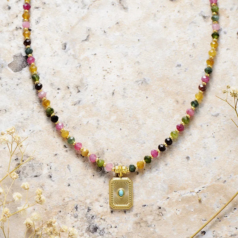 Necklace with multicolored beads and a gold pendant on a textured surface